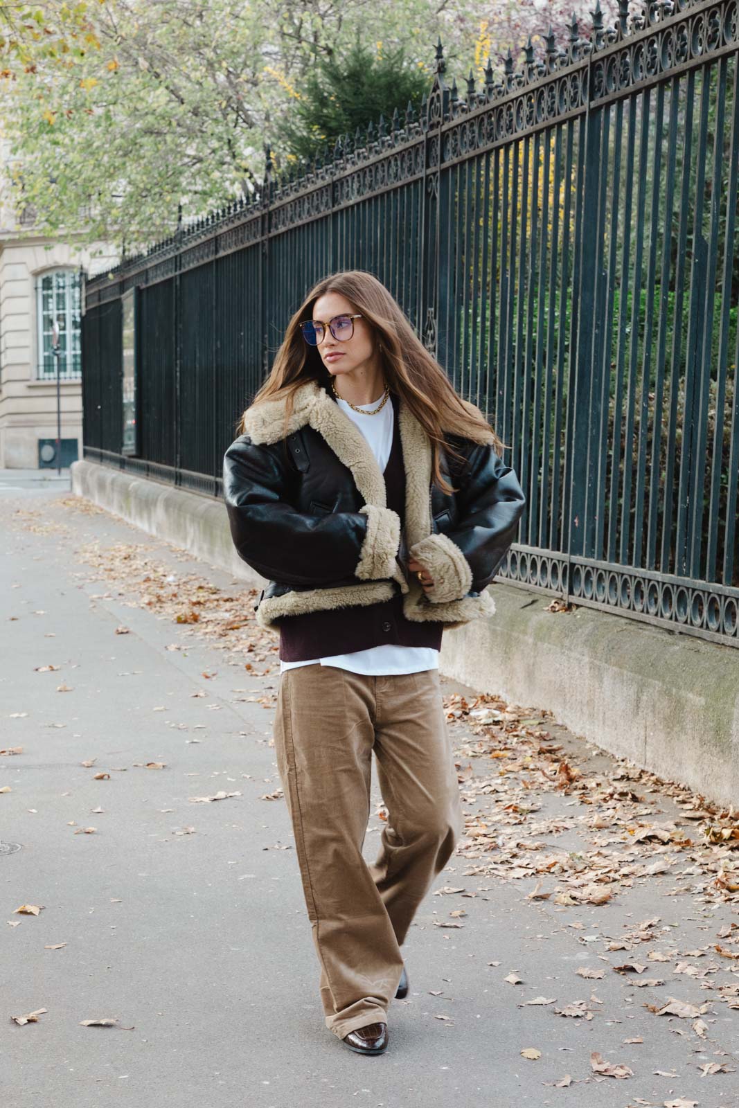 אישה צעירה בלבוש חורפי אופנתי, מעיל דמוי עור עם פרווה ומכנסי קורדורוי רחבים ברחוב עירוני