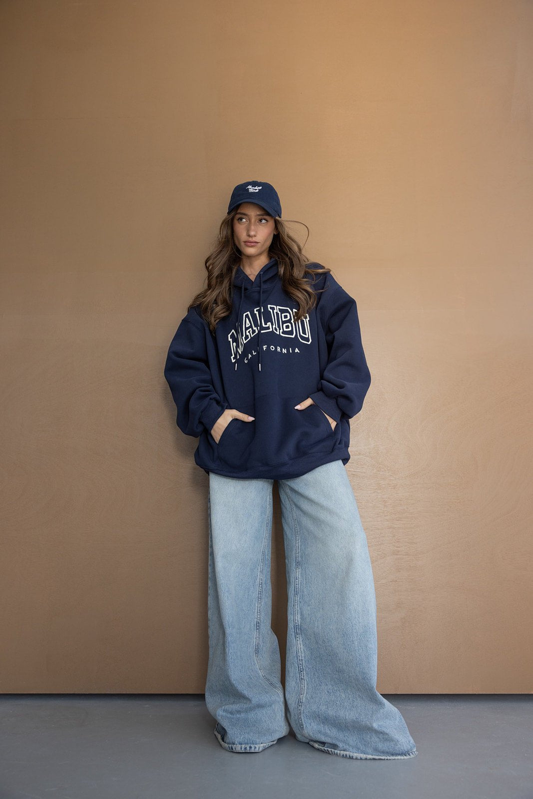 אישה צעירה עם קפוצ'ון כחול ומכנסי ג'ינס רחבים, לוק קז'ואל אופנתי לנשים ולנערות