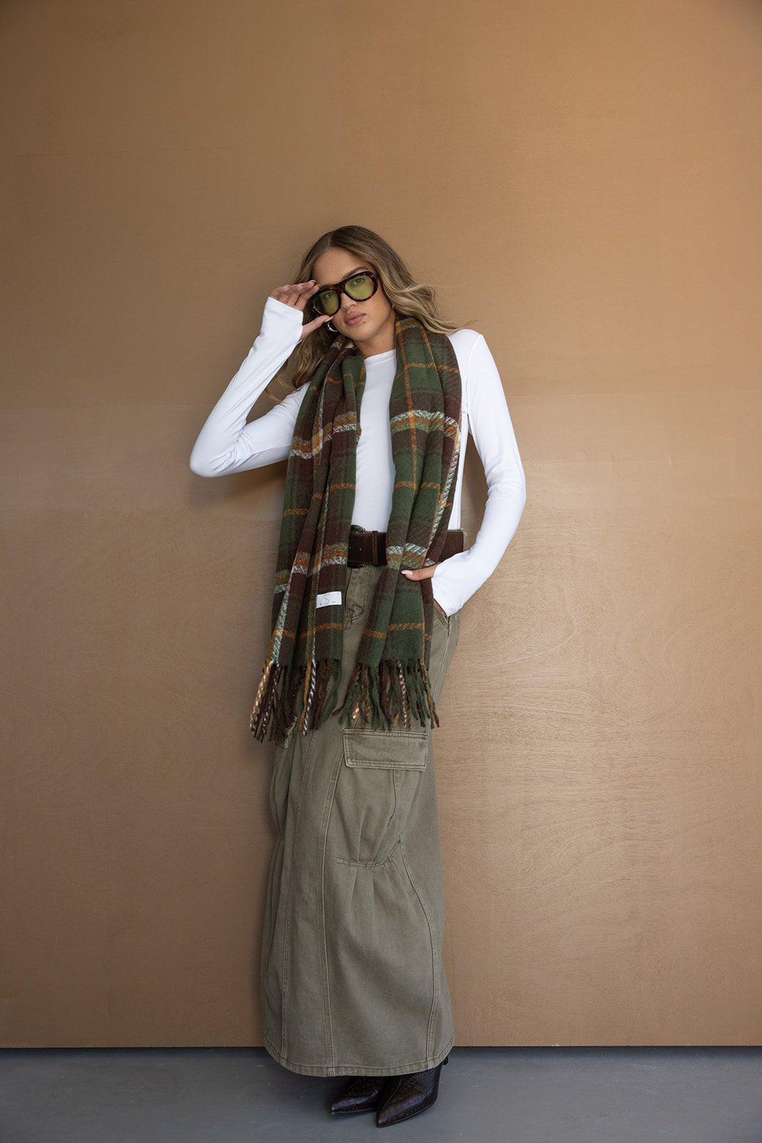 דוגמנית עם צעיף משובץ ירוק-חום, חולצה לבנה ארוכה, חצאית ירוקה ומשקפי שמש אופנתיים