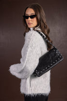 אישה עם משקפי שמש, לובשת סוודר פלאפי אפור ותיק צד עור שחור עם ניטים, אופנה לנשים