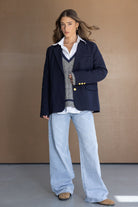 דוגמנית לובשת בלייזר כחול כהה, ג'ינס רחב, סוודר אפור וחולצה לבנה, אופנת נשים טרנדית