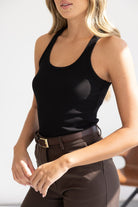 אישה לובשת גופייה שחורה מחטבת ומכנסיים חומים עם חגורה, אופנת קיץ לנשים ונערות