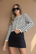 אישה בלבוש אופנתי, חצאית שחורה קצרה וסוודר פסים, משקפי שמש, רקע חום