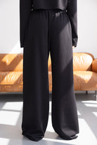 מכנסיים רחבות לנשים בצבע שחור, בד נעים ונופל, צילום באור טבעי על רקע ספה