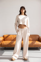 אישה לובשת סט טרנינג אופנתי בצבע שמנת עם כובע בסיסי, יושבת על ספה חומה, אופנת נשים צעירה