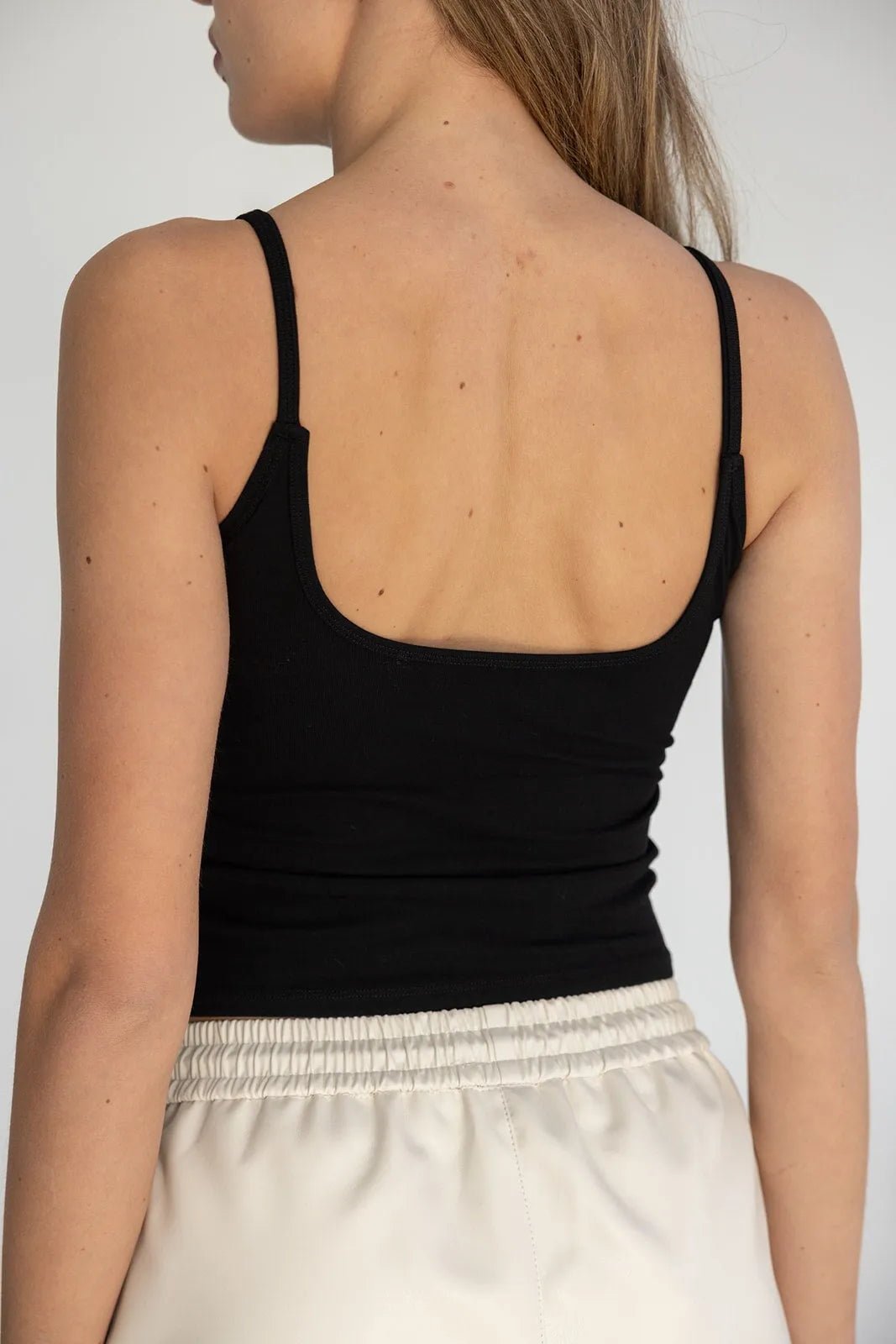 גופיית נשים שחורה עם כתפיות דקות, גב פתוח, בשילוב מכנס לבן קייצי