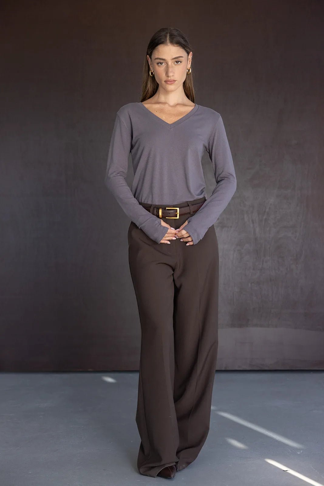 אישה לובשת חולצת וי ארוכה אפורה ומכנסיים מחויטים חומים, אופנה לנשים צעירות