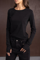 דוגמנית לובשת חולצה שחורה ארוכה ומכנסיים שחורים אופנתיים, רקע חום