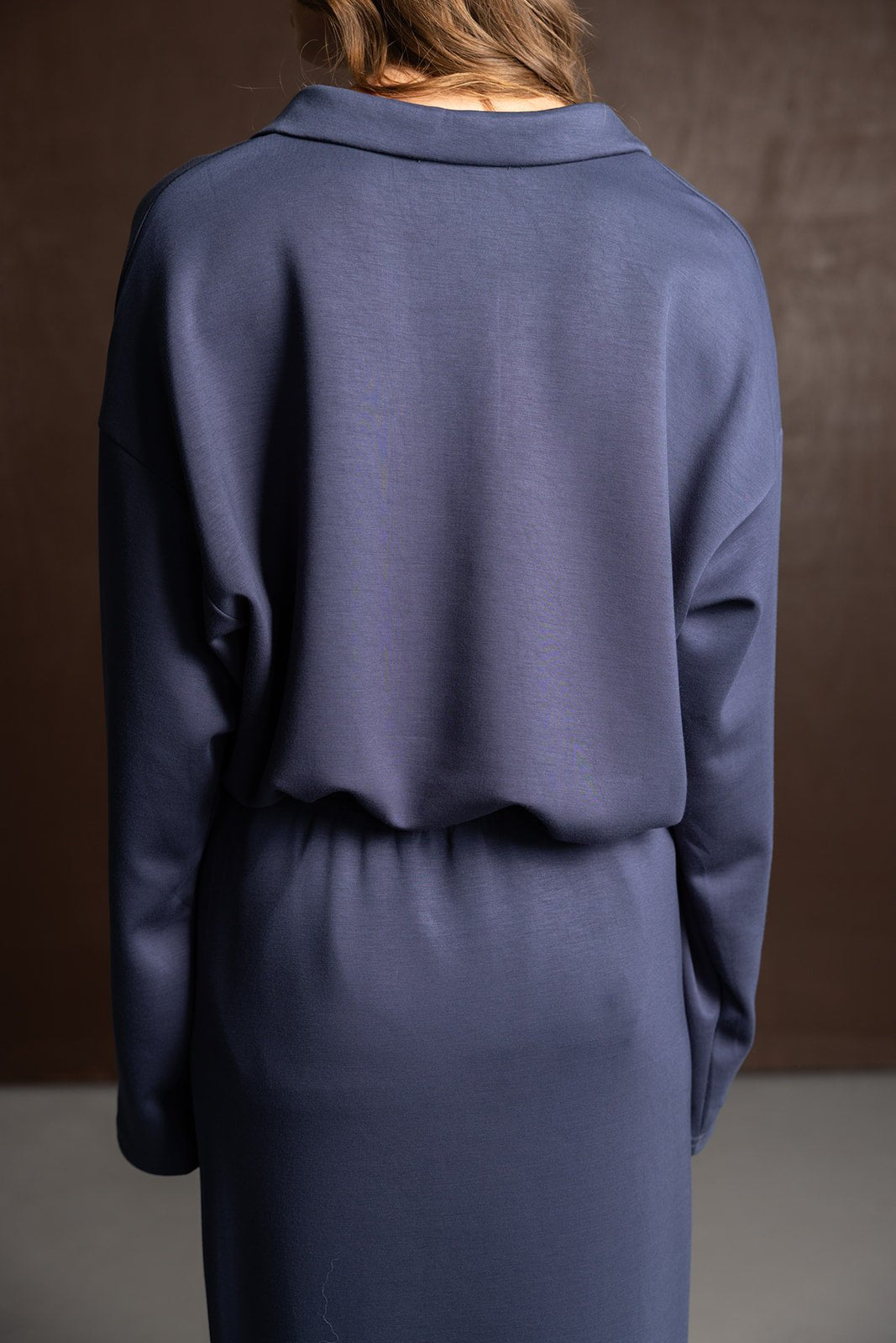 שמלת נשים כחולה בגזרה נינוחה עם שרוולים ארוכים, מצולמת מאחור על רקע כהה