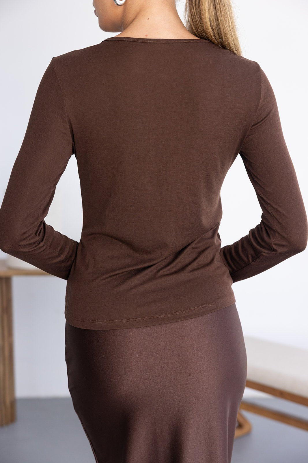 חולצת נשים חומה ארוכה בגזרה צמודה, מבד חלק, מצולמת מאחור, אופנה לנשים