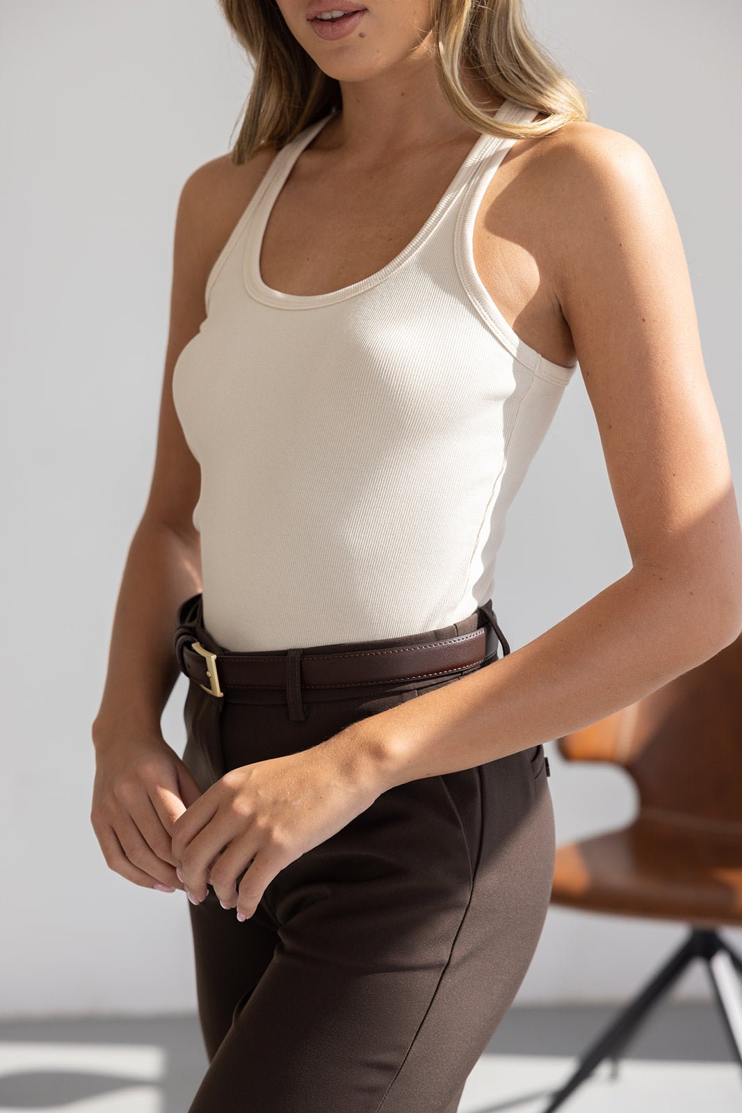 אישה לובשת גופיית סריג בז׳ ומכנסיים חומים מחויטים עם חגורה, אופנת נשים קיץ