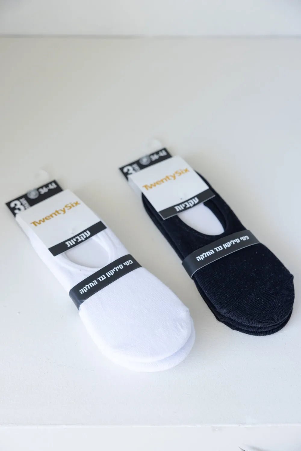 זוגות גרבי עקביות לנשים בצבעי לבן ושחור, על משטח לבן, ארוזות באריזה ממותגת