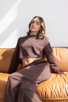 דוגמנית יושבת על ספה עם חליפת טרנינג חומה, אופנת נשים ונערות, לוק קז'ואל מחמיא