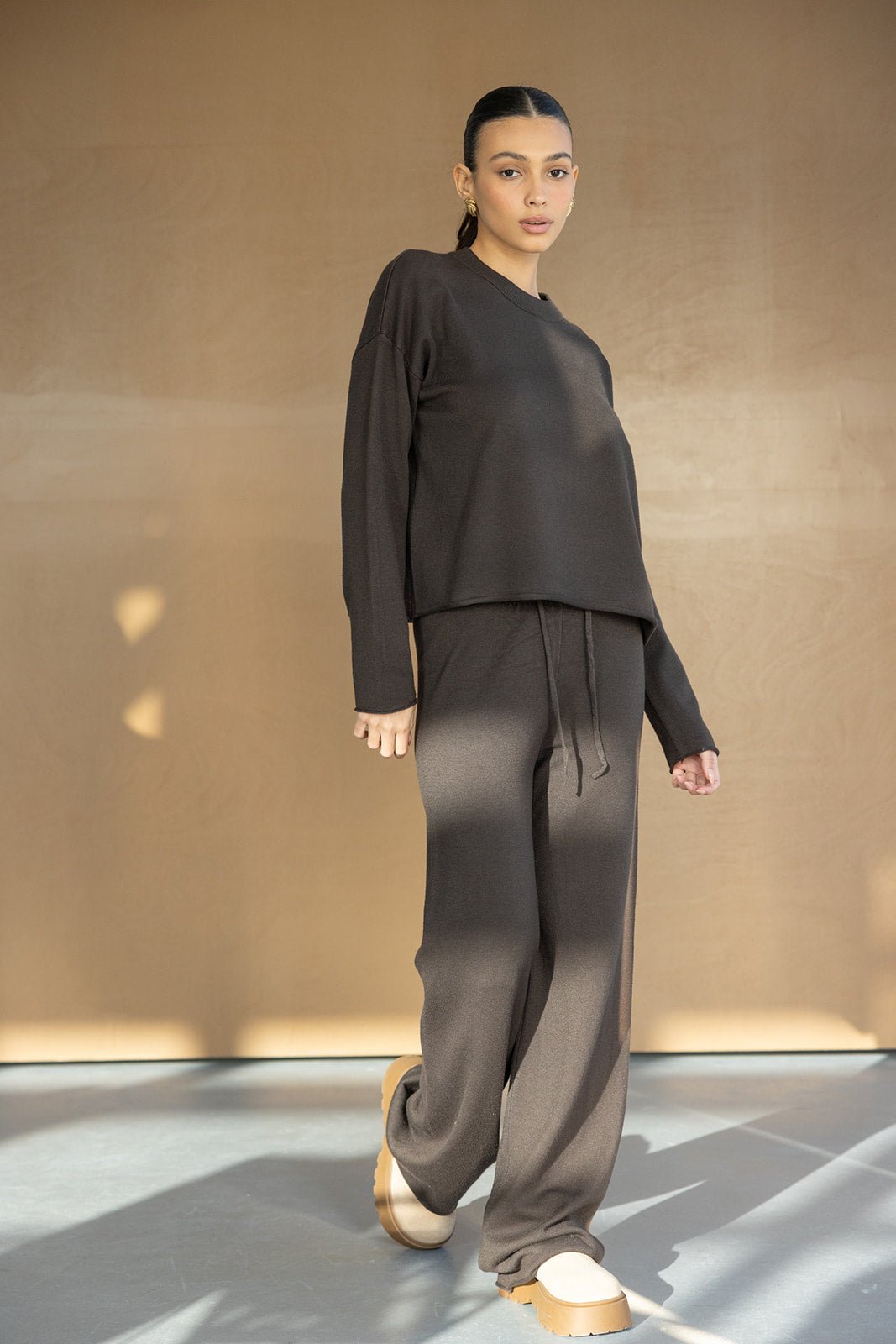 אישה צעירה לובשת סט בגדי טריקו אלגנטי בגוון חום כהה, חולצה ארוכה ומכנסיים רחבים, אופנה לנשים