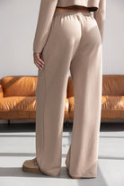 מכנסי נשים רחבים בגזרה גבוהה בצבע בז', בסגנון קז'ואל, מצולמים על רקע ספה חומה