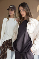 שתי נשים לובשות בגדים אופנתיים בסגנון קז'ואל לנוער, אחת עם ג'קט בז' ומכנסיים כהים, השנייה בלבן וכובע מצחיה