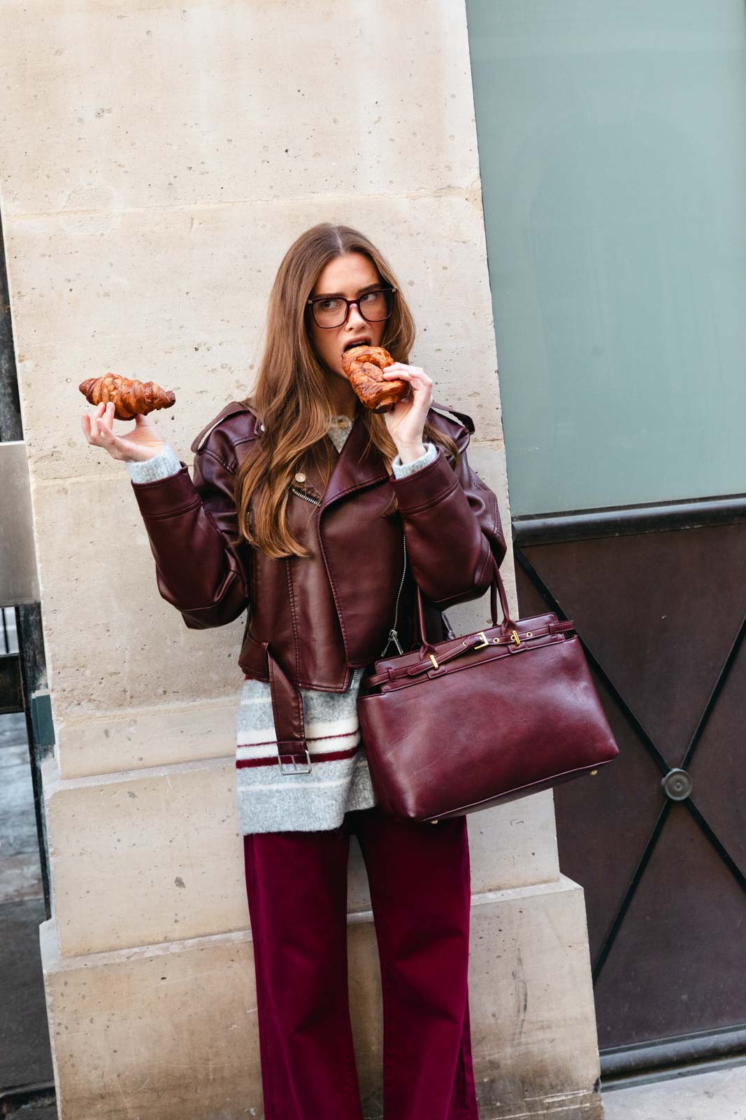 אישה אופנתית עם מעיל בורדו ותיק תואם, אוכלת קורסון ברחוב עירוני