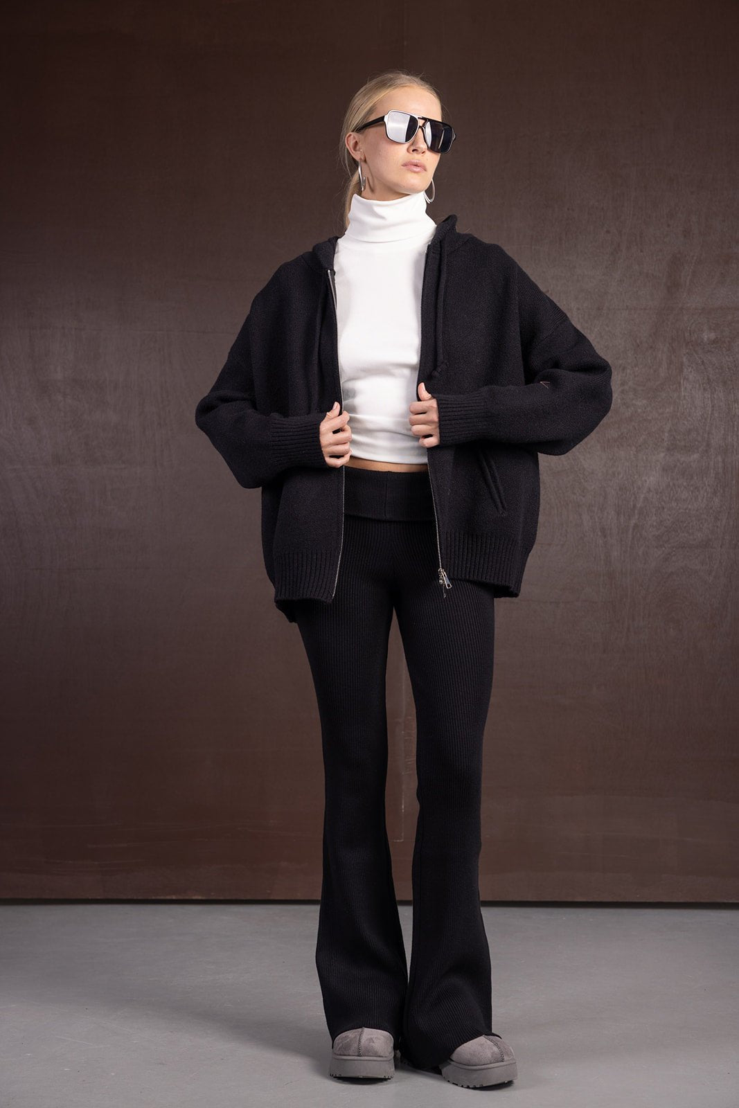 אישה לובשת ג'קט בייסיק שחור, מכנסיים מחויטים שחורים, גולף לבן ומשקפי שמש אופנתיים