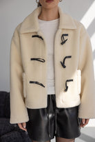 בלוק חורפי אופנתי לנשים, דוגמנית עם מעיל פרווה לבן קצר, סוגרי פלסטיק שחורים, חצאית דמוי עור שחורה