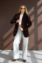 אישה עם בלייזר קטיפה חום, ג'ינס בגזרה רחבה, חולצה לבנה קצרה ומשקפי שמש אופנתיים