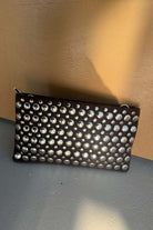 קלאץ' אופנתי לנשים בצבע שחור עם ניטים כסופים, תיק ערב מעוצב מונח על רקע בהיר