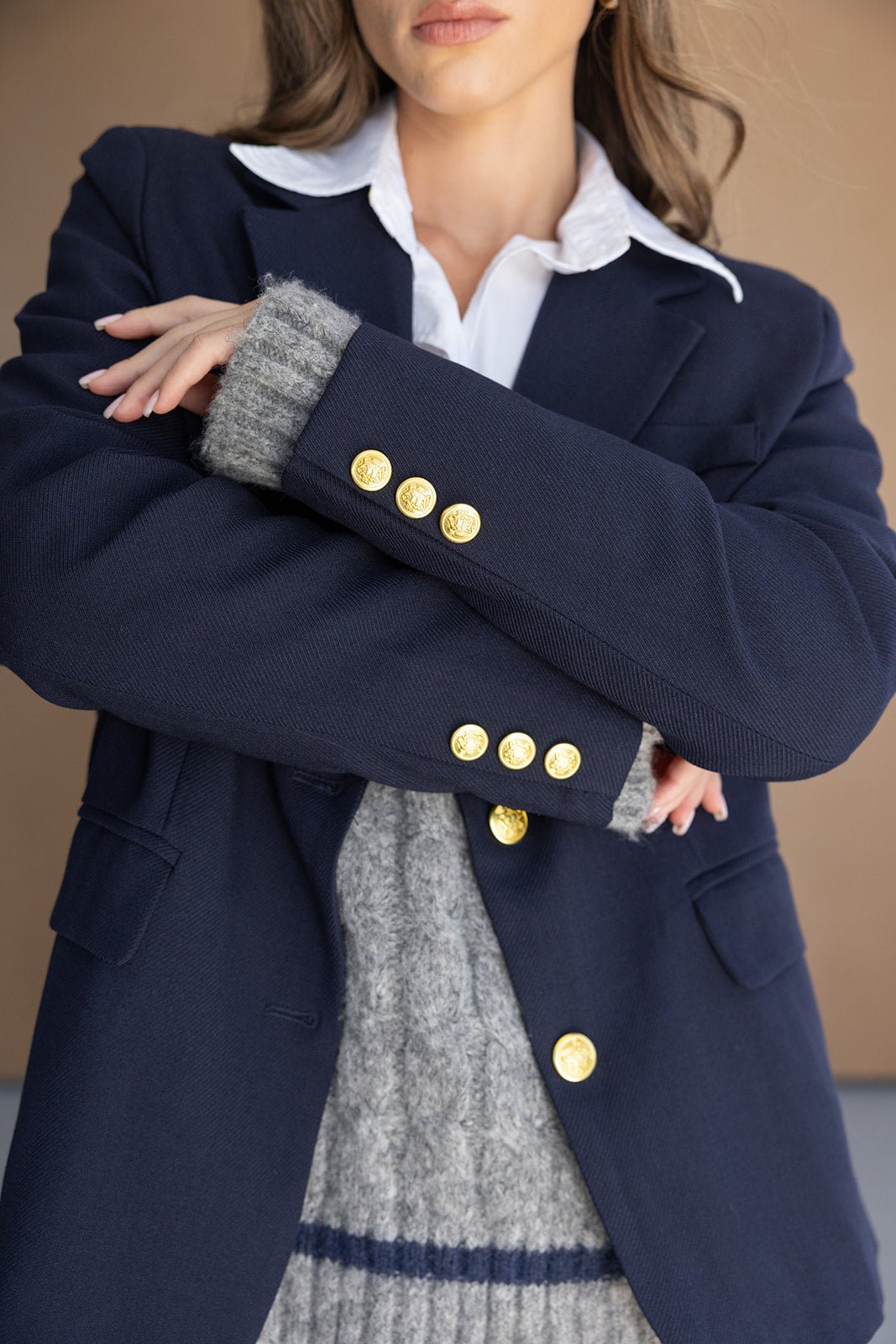 אישה לובשת בלייזר כחול עם כפתורים מוזהבים, חולצה לבנה וסוודר אפור, אופנת נשים חורפית אלגנטית