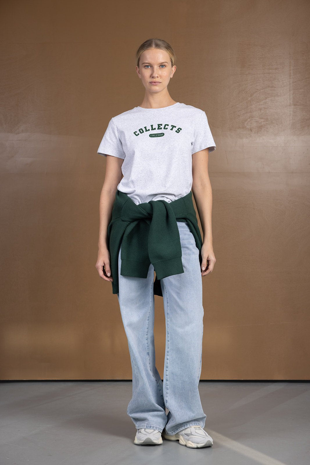 אישה עם חולצת טי שרט אפורה עם הדפס, מכנסי ג'ינס רחבים, וסוודר ירוק קשור במותן, אופנת רחוב לנשים