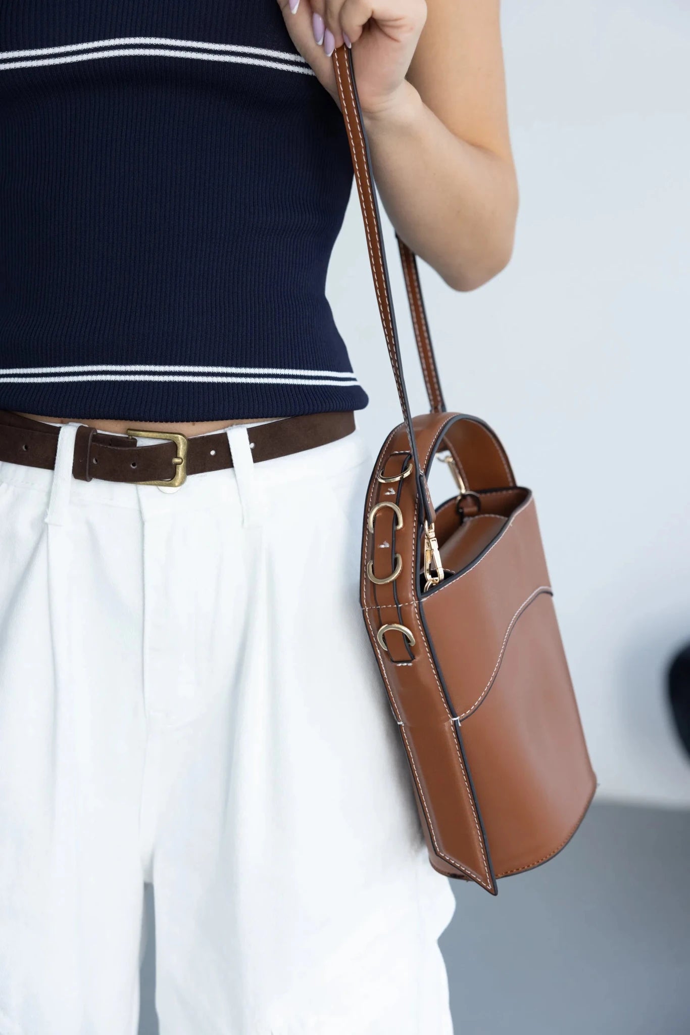 אישה עם מכנסיים לבנים, גופיית קיץ כחולה ותיק צד חום אופנתי