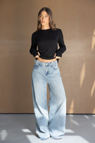 אישה צעירה לובשת חולצה שחורה וג'ינס רחב בגזרת באגי, אופנת נשים עדכנית, רקע נייטרלי