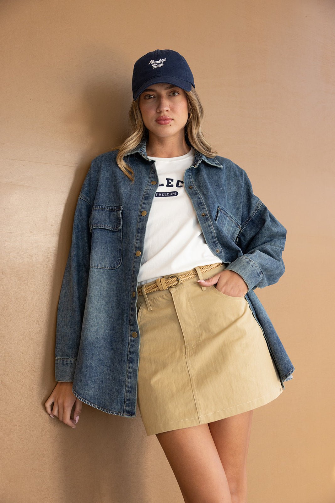 אופנת נשים קז'ואל: דוגמנית עם חולצת ג'ינס, חצאית מיני בז', כובע קז'ואל וחולצה לבנה