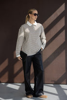 אישה לובשת חולצת פסים עם צווארון לבן, מכנסי עור שחורים, משקפי שמש ותיק קלאץ', אופנה לנשים