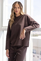 אישה לובשת סט טרנינג חום ארוך, אופנה לנשים, צילום באור טבעי ליד חלון