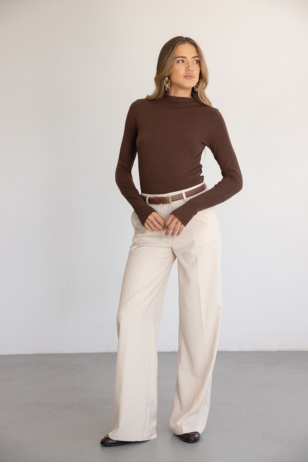 אישה לובשת חולצה חומה ארוכה ומכנסיים רחבים בגוון בז', לוק אופנתי לנשים