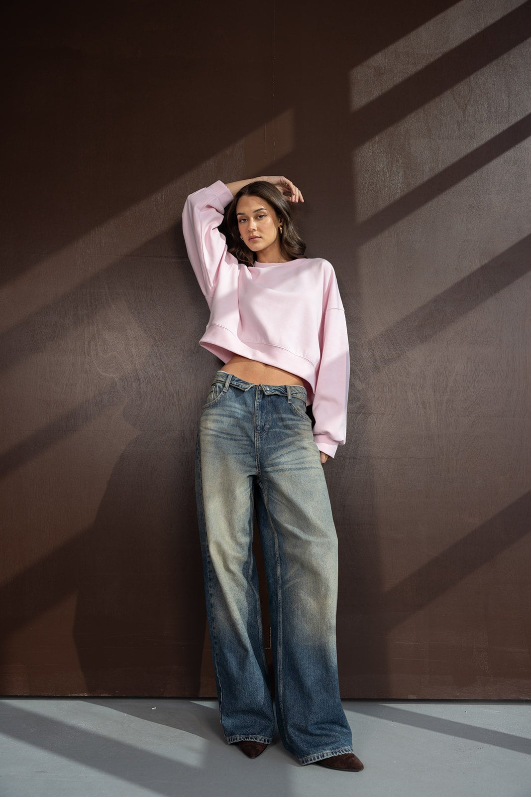 דוגמנית לובשת סווטשירט ורוד קצר ומכנסי ג'ינס רחבים, אופנת נשים צעירה וטרנדית