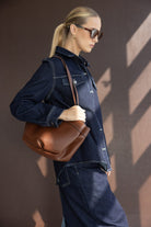 אישה לובשת ג'קט ג'ינס כהה עם תיק כתף חום אופנתי ומשקפי שמש, מראה אופנה עדכנית