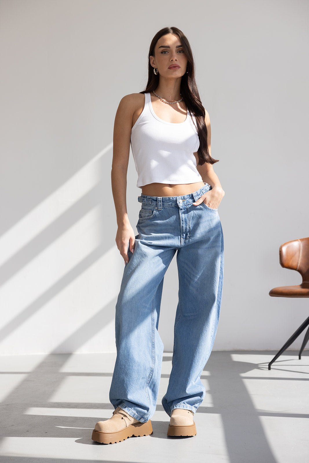 דוגמנית לובשת גופייה לבנה קצרה ומכנסי ג'ינס רחבים אופנתיים לנשים, צילום בסטודיו מואר