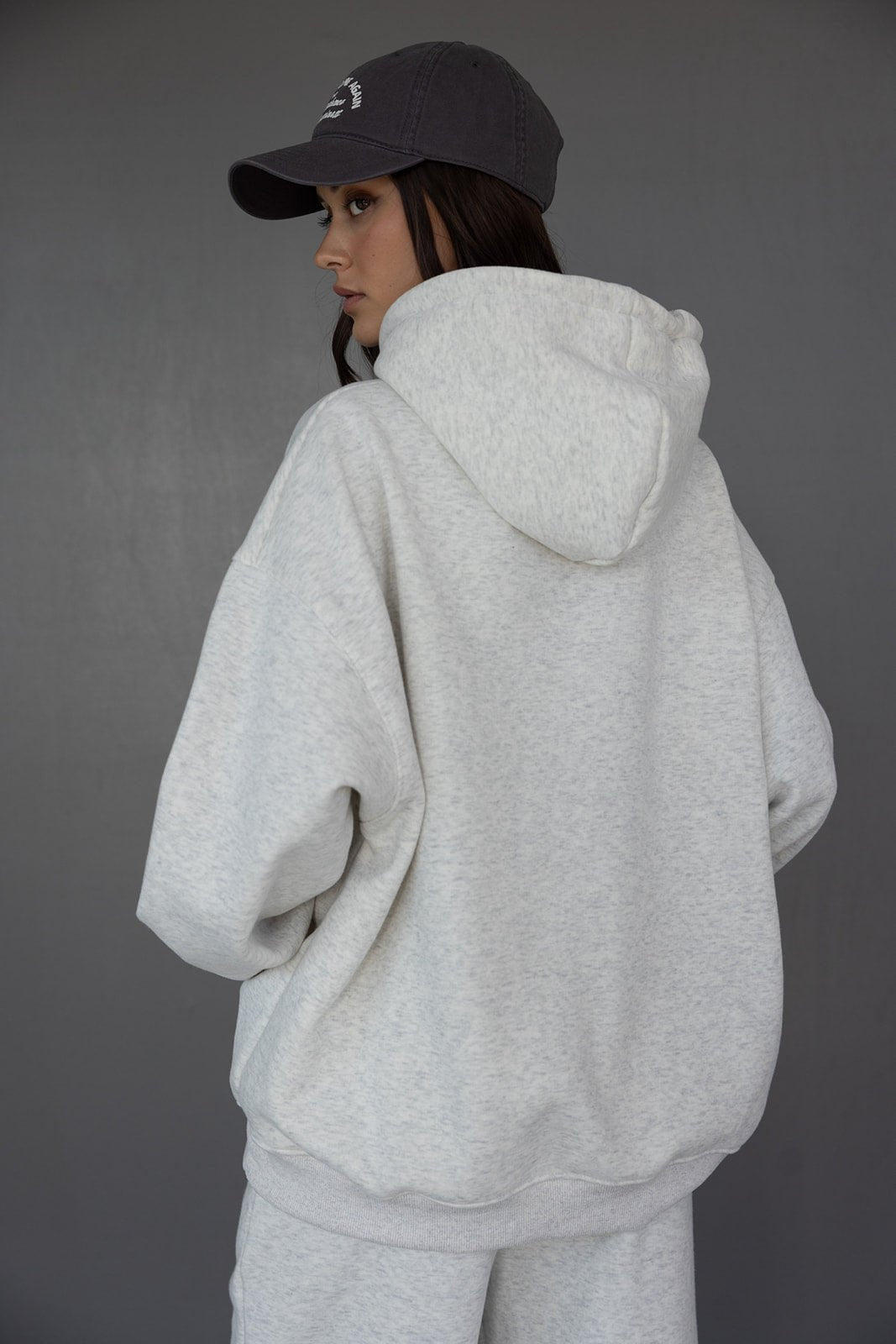 אישה צעירה עם קפוצ'ון אפור וכובע מצחייה שחור, לוק ספורטיבי אופנתי לנשים