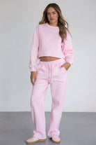 דוגמנית לובשת סט טרנינג ורוד לנשים, כולל סווטשירט קצר ומכנסיים ארוכים, אופנת רחוב נוחה