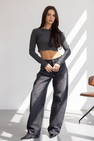 דוגמנית לובשת גופיית קרופ אפורה עם שרוולים ארוכים ומכנסי ג'ינס רחבים באופנת רחוב לנערות