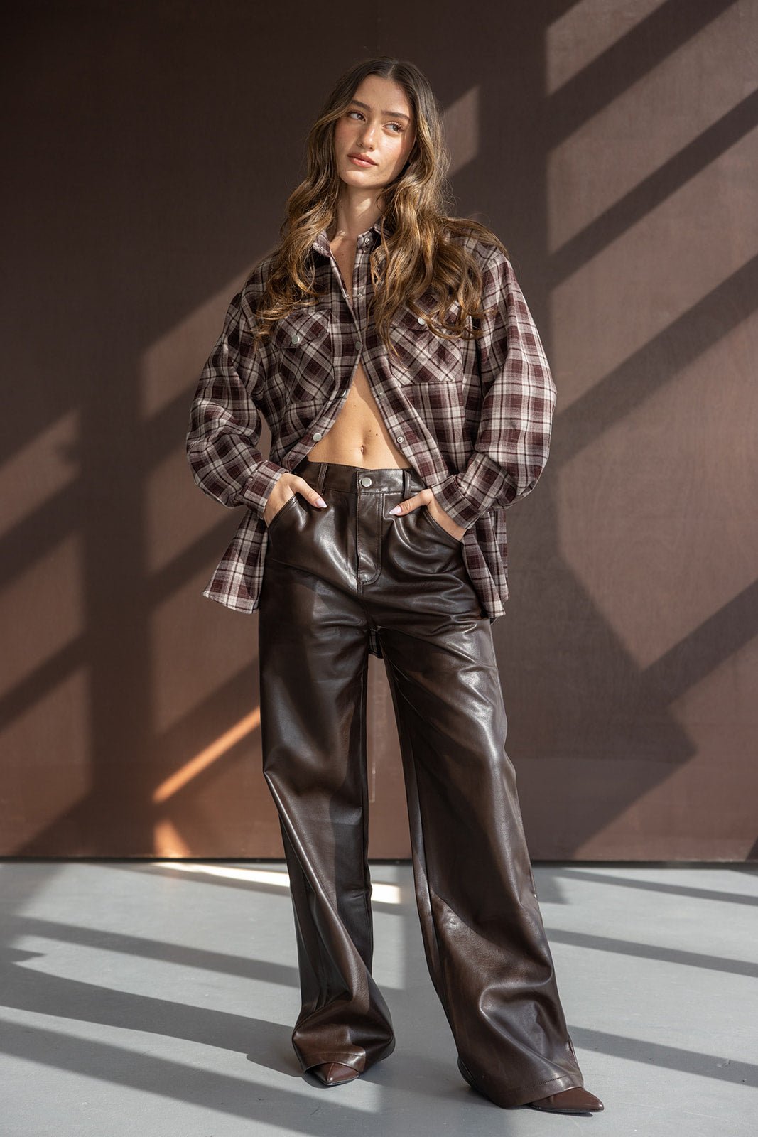 דוגמנית לובשת חולצה משובצת חומה ומכנסי עור רחבים חומים, אופנה לנשים צעירות