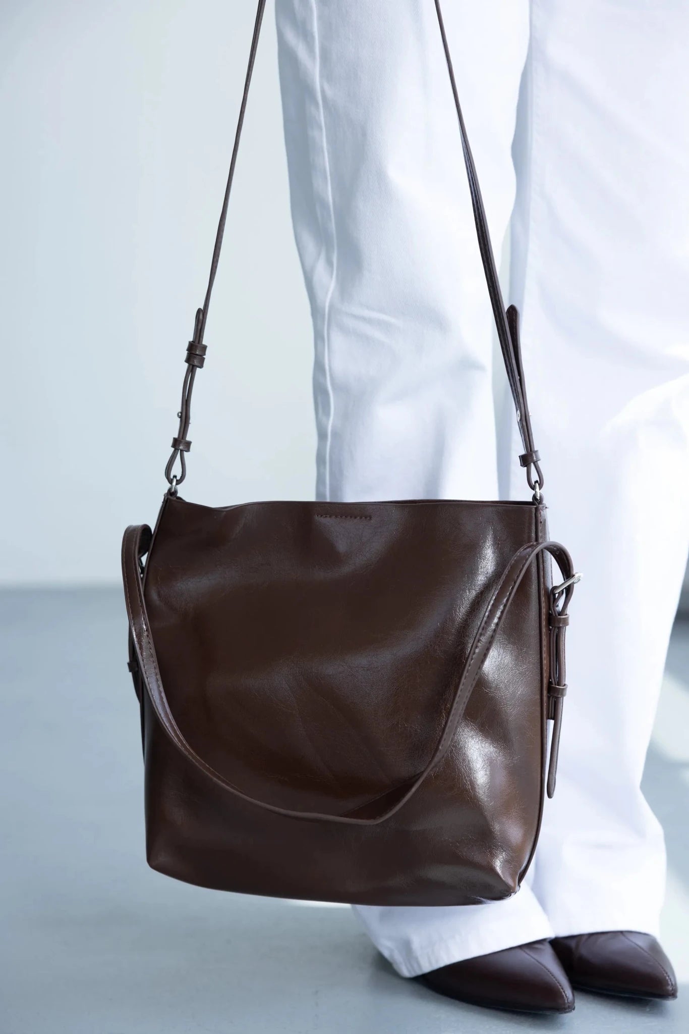 תיק צד חום לנשים עם רצועה ארוכה, ליד מכנסיים לבנים ונעלי עקב חומות, אופנה לנשים