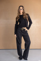 אישה עם ג'קט שחור ומכנסיים שחורים רחבים, משקפיים אופנתיים, מראה אופנה לנשים צעירות