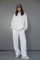 אופנת נשים: דוגמנית לובשת סט טרנינג אפור, קפוצ'ון ומכנסיים רחבים, כובע מצחייה אפור ונעלי סניקרס