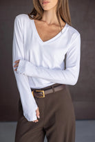 חולצת נשים לבנה עם שרוול ארוך ומחשוף וי, משולבת עם מכנסיים חומים מחויטים וחגורה.