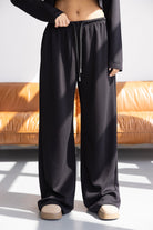 מכנסיים שחורים רחבים לנשים עם מותן אלסטית, בצילום אופנתי ליד ספה חומה