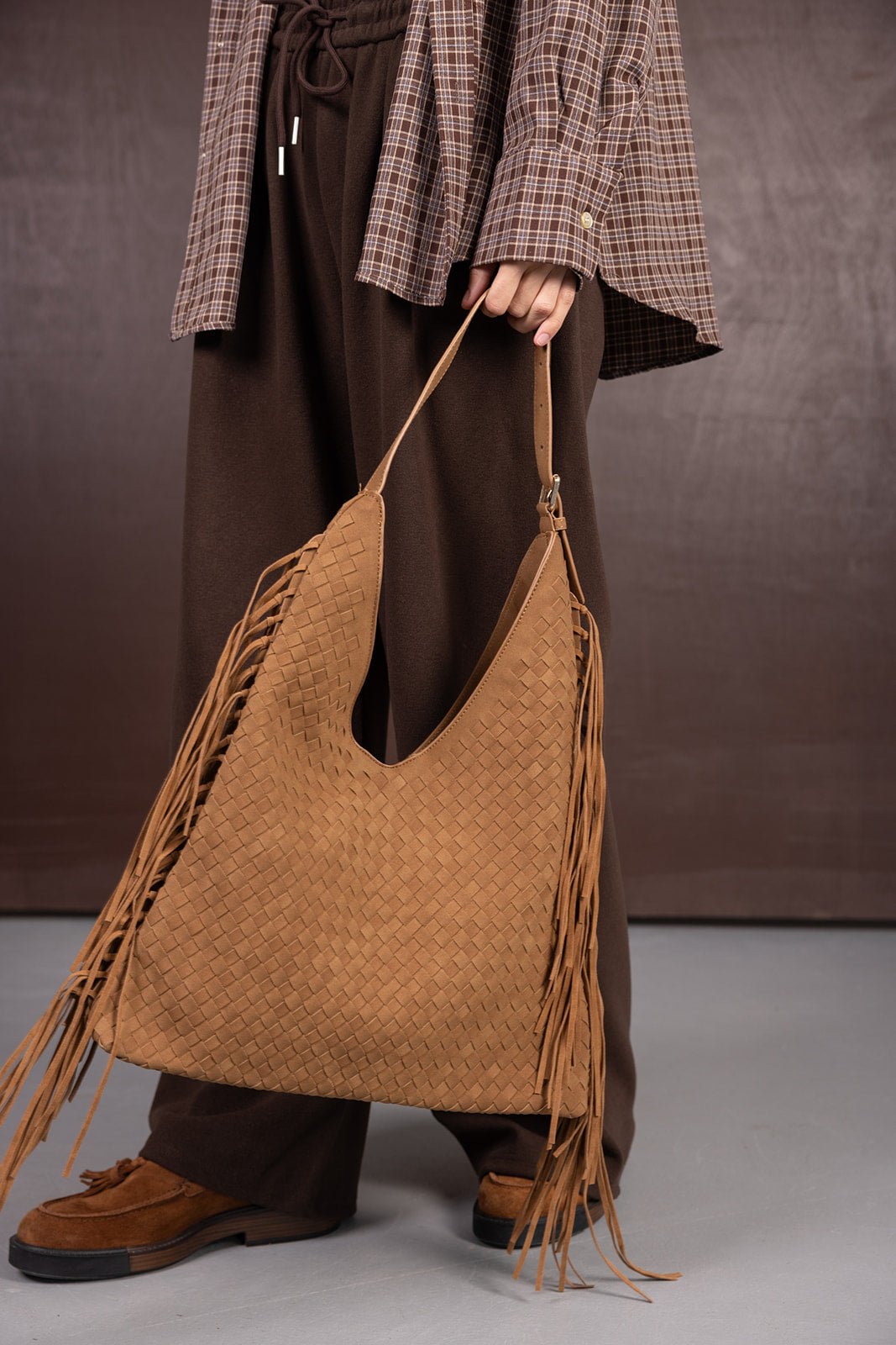 תיק חום קלוע עם פרנזים, משולב עם מכנסיים חומים וחולצה משובצת אופנתית לנשים