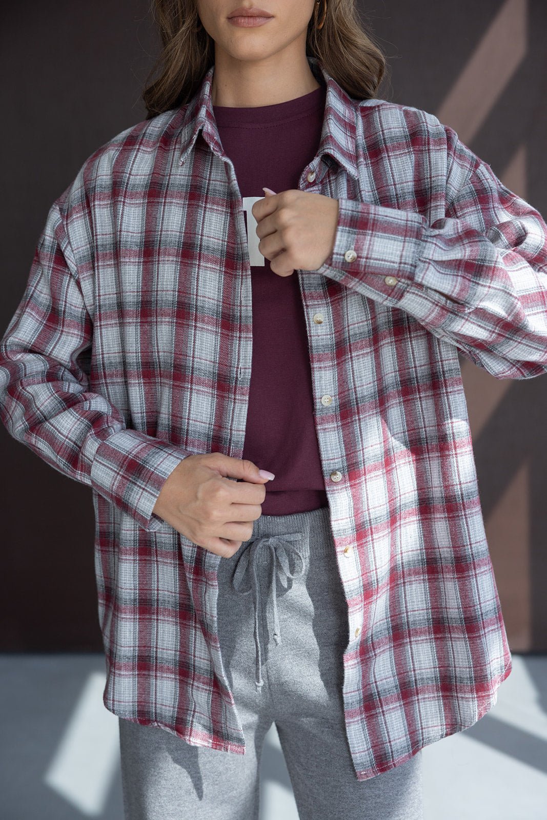 חולצת פלאנל משובצת באדום ואפור לנשים, מעל טי שירט בורדו ומכנסי טרנינג אפורים
