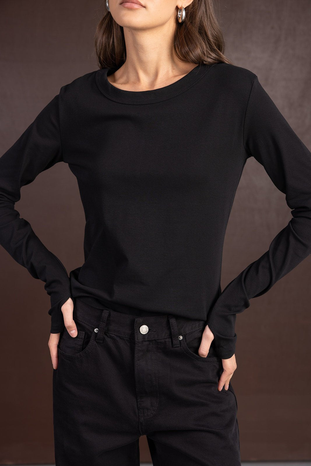 אישה לובשת חולצה שחורה ארוכה ומכנסי ג'ינס שחורים, אופנת נשים צעירה ואלגנטית