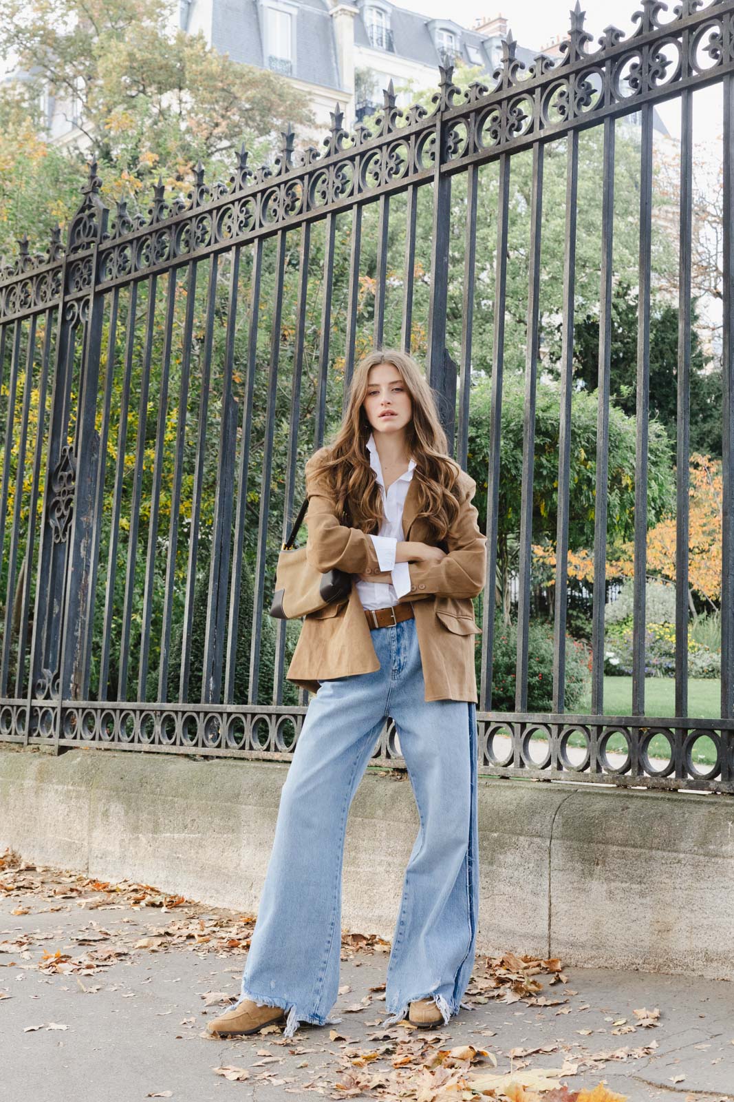 דוגמנית צעירה לובשת ז'קט חום וחולצה לבנה עם ג'ינס רחב, מצולמת ברחוב עירוני בצילום אופנה סתווי