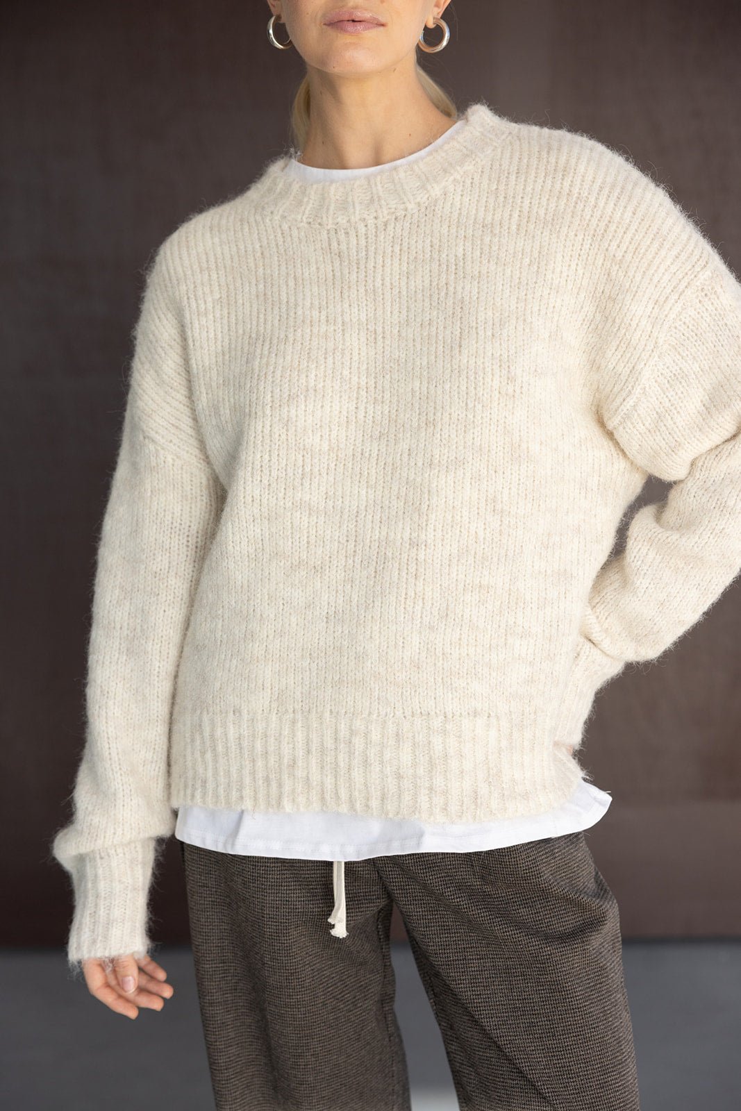 אישה לובשת סוודר צמר שמנת אופנתי לנשים עם חולצה לבנה ומכנסיים מחויטים